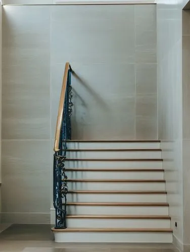 A side view of a staircase with dark wooden steps and an ornate golden railing. The railing features intricate, swirling designs inspired by nature, with elegant curves and small decorative elements l