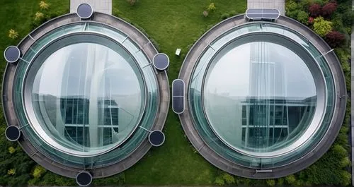 an aerial top view of two modern public buildings connected by a paved walkway. The buildings should feature sleek glass facades and concrete materials, seamlessly blending into a beautifully landscap