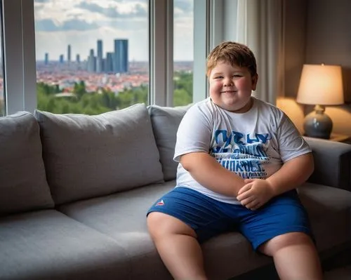 Pudgy Roberts, chubby boy, 10yo, messy brown hair, freckled nose, bright blue eyes, smiling face, casual wear, white graphic t-shirt, dark blue shorts, sneakers, sitting on a couch, living room, moder