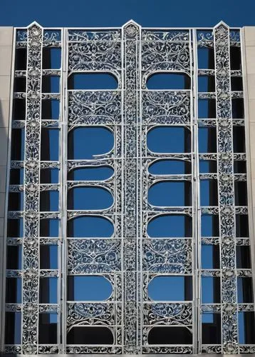 ornate architectural grille, AG10, modern building facade, intricate metal patterns, silver finish, geometric shapes, symmetrical composition, urban cityscape, high-rise buildings, daytime, clear blue