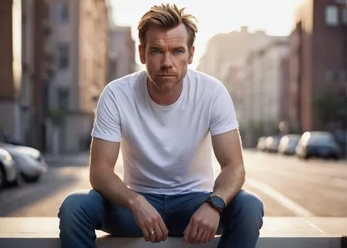 Ewan McGregor, blue eyes, piercing gaze, masculine facial features, short brown hair, subtle stubble, casual smile, relaxed posture, plain white T-shirt, fitted jeans, brown leather belt, sneakers, ur