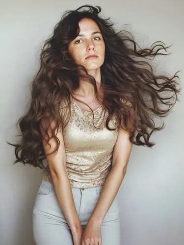 a woman with long, wavy brown hair,the woman in gold shirt is standing near a wall,voluminous,pelo,longhaired,long hair,gypsy hair,curly brunette,Photography,Documentary Photography,Documentary Photog