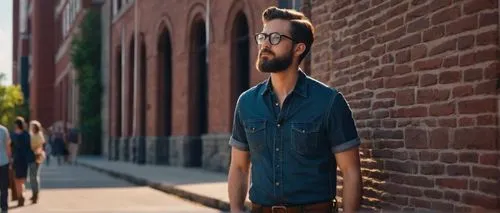 Male photographer, 30s, hipster style, black framed glasses, short brown hair, casual beard, Nikon camera, leather strap, dark blue denim jeans, brown boots, standing, leaning against a stone wall, ca