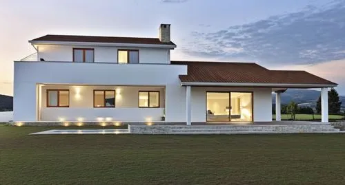 A modern, minimalist white house with clean lines and a few stone accents on the façade. The porch features white beams, complementing the sleek, minimalist design. The house is slightly elevated abov