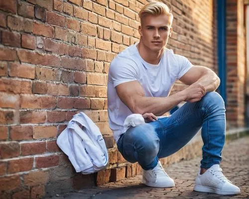 Handsome Andreas, young adult male, blond hair, blue eyes, fit physique, casual wear, denim jeans, white T-shirt, sneakers, relaxed posture, leaning against, brick wall, urban setting, afternoon sunli