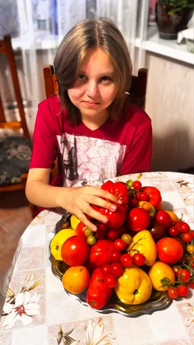 a girl holding a bunch of tomatoes in front of a pile of fruit,tomates,roma tomatoes,tomatoes,tomatis,grape tomatoes,bellpepper