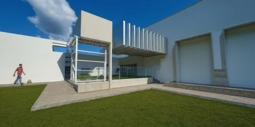 AREA DE CONVIVENCIA, CON PERGOLAS DE CONCRETO, LOSA CON REMATE DE VIGA DE ACERO, ESPEJO DE AGUA ,a woman walking towards a tall white building on a bright day,modern house,cubic house,siza,modern arch