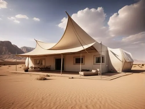 A clay-colored caravan resembling traditional Saudi mud houses, with white-framed windows and door, accompanied by an awning, is set in the desert with a backdrop of rocky mountains.,dunes house,admer