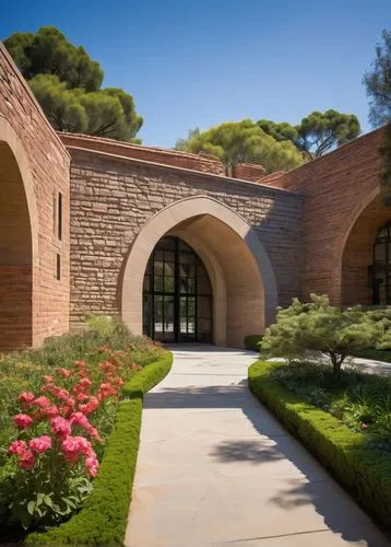 Arc-shaped building, UCLA campus, sunny day, blue sky, few white clouds, lush green trees, vibrant flowers, walking path, stone pavement, modern architecture, glass windows, steel frames, minimalist d