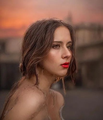 the image depicts a woman with long brown hair, deep-set brown eyes, and fiery red lips as she gazes up at the sky, lost in thought. The sky is painted in colors of white and pink, as the sun slowly r