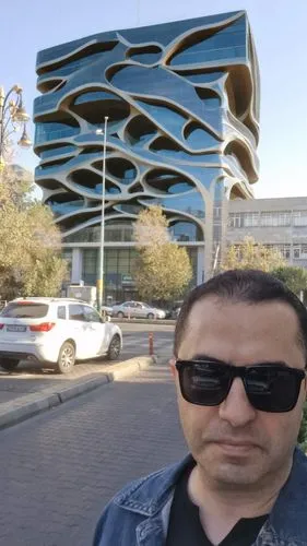 Amazingparametric  building, trade center design ispired by Zaha Hadi architecture,,a man with sunglasses and denim jacket standing in front of a blue building,kaust,masdar,arbil,sulaymaniyah,irbil,zo