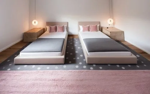 A cozy room for two girls, with a gray bed, and pink bedspreads, gray decorative pillows, a stuffed rabbit on them, the floor is dark brown and matches the bedside tables, all the walls are white, and