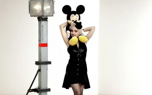 Madonna is on a movie set and she has Mickey Mouse on her shoulders. Madonna is wearing a sexy dress and has beautiful legs and she is wearing high heels. The movie set is full of crew members such as