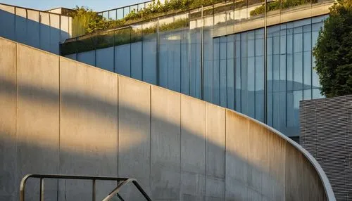 Ramp architecture, modern, sleek, minimalist, concrete structure, geometric shapes, clean lines, brutalist style, industrial feel, urban setting, cityscape, evening time, warm golden lighting, dramati