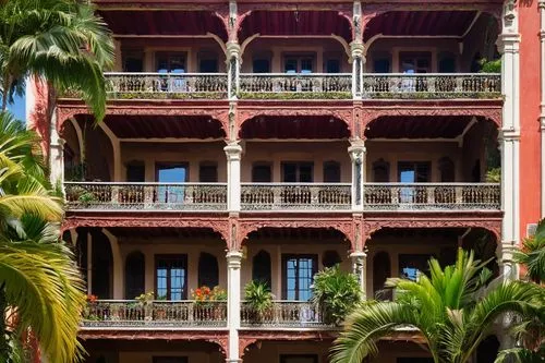 Neo-colonial building, grandiose, ornate facade, intricate stonework, arched windows, balconies with iron railings, red-tiled roof, lush greenery, palm trees, vibrant flowers, sunny day, warm lighting