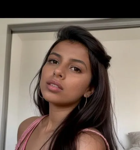 The Moroccan girl with her lips pursed for a kiss and she blows into her palm.  She is sitting on the bed in her room.  She wears a short pink blouse.,a close - up of a woman's face and chest,thahane,