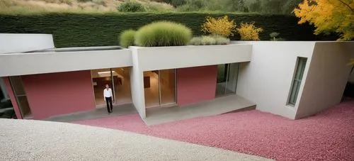 DISEÑO EXTERIOR DE UNA CASA ESTILO MINIMALISTA, CON ELMENTOS DE COLOR BLANCO, COLOR CONCRETO PULIDO, UN MURO EN COLOR ROSA MEXICANO, TERRENO CON PENDIENTE CON CESPED, FOTOGRAFIA HIPERREALISTA, VEGETAC