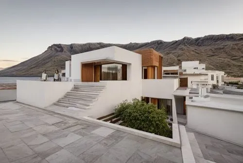 “Rear view of a modern house. First module with white walls and wood siding. Second module with oak wood color panels.” “At the back, there is an old volcano mountain in the northwest of Tenerife.”,ro