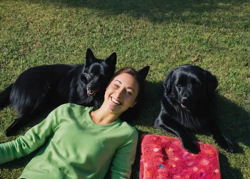 smiling woman lying on ground beside black dog at daytime,flat-coated retriever,gordon setter,giant schnauzer,afghan hound,beauceron,pet vitamins & supplements,bosnian coarse-haired hound,istrian coar