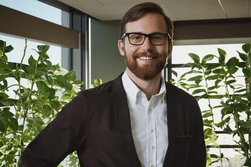 Happy, smiling Douglas Seidler, 2018 Revit Architecture designer, male, casual wear, black glasses, short brown hair, beard, standing, hands in pockets, relaxed pose, modern office interior, wooden de