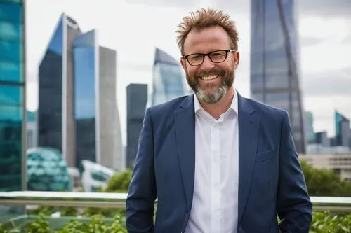 Middle-aged man, suit, glasses, short brown hair, beard, smiling, confident pose, standing in front of a city skyline model, hands behind back, skyscraper, modern architecture, glass and steel structu