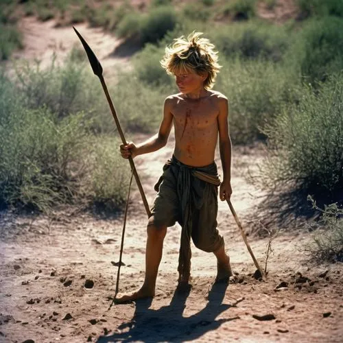 Shirtless sunburn barefoot filthy dirty angry young boy in the wild holding a spear with messy hair covered in sweat dirt and scars in bright sunshine in blazing heatwave sneaking around hunting in th