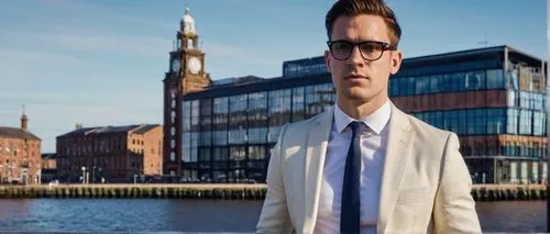 Male, architectural designer, 30s, casual business attire, black framed glasses, short brown hair, light stubble, white dress shirt, dark blue blazer, fitted trousers, black leather shoes, holding a l