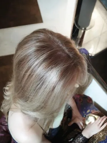 the view is from above the woman is sitting sideways and has long hair, keep her hands the same,hair coloring,blonde woman reading a newspaper,blond hair,blonde sits and reads the newspaper,short blon