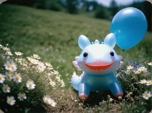 Axolotl, balloon animal, colorful inflated body, transparent fins, shimmering scales, bright blue eyes, party hat on head, holding a tiny bouquet of flowers, sitting on a grassy hill, surrounded by bl