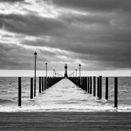 a long pier extending into the ocean under a cloudy sky with a lighthouse in the distance on a cloudy day, Derold Page, art photography, award - winning photography, a black and white photo,old pier,c