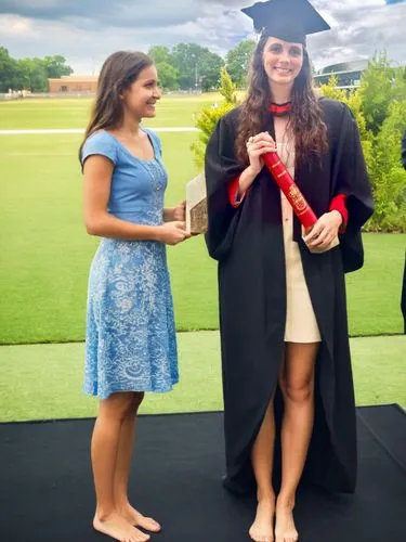 A barefoot girl receives the university award and her professor stands next to her.,a lady holding a red book with a red tassel,degrees,college graduation,graduated,graduale,degree,graduations