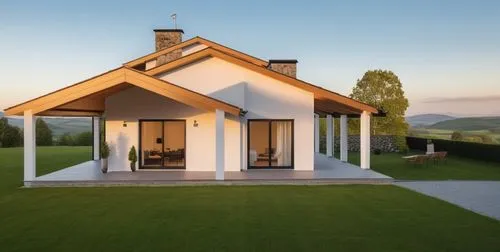 A minimalist Scandinavian-style house with a gable roof, featuring stone details on the facade, set in a quaint village surrounded by small hills and forest. The house has large windows with black fra