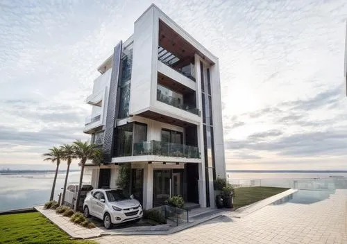 there is a car parked in front of the building,house by the water,penthouses,damac,waterview,luxury property,residential tower,aldar,belek,cube house,modern architecture,cubic house,baladiyat,lekki,mo