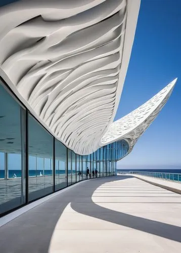 Wavy roof, futuristic building, undulating structure, white concrete walls, glass windows, reflective surface, ocean-inspired design, seaside location, sunny day, blue sky, seagulls flying overhead, p