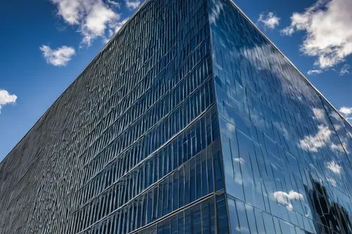 Modern FedEx office building, sleek glass façade, silver metal frame, minimalist architecture, clean lines, angular shapes, urban cityscape, daytime, blue sky, few puffy white clouds, detailed reflect