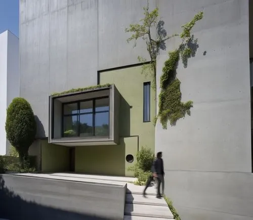 In a futuristic minimalist architecture, the house stands tall against a backdrop of bold, dark buildings. Its walls are bare, with deep, rich shades of green contrasting against the stark backdrop. T