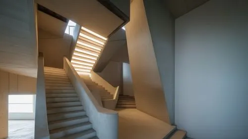 Stairwell with light pouring in from above.  The material is concrete. Light permeating from the walls,a long stair way leading up into a room,winding staircase,staircase,staircases,stairwell,stairwel