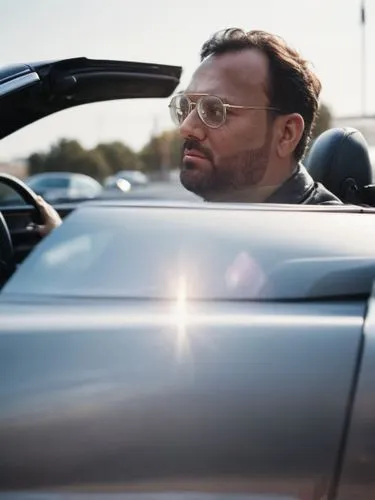 a man with glasses sits in his car in a parking lot,kunchacko,giamatti,diamantopoulos,rimac,veyron,domenicali