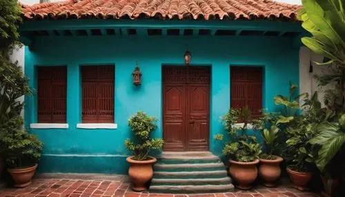 South American architecture, colorful colonial-style building, vibrant turquoise walls, ornate wooden doors, intricate stone carvings, red-tiled rooftops, sprawling verandas, lush greenery, potted pla