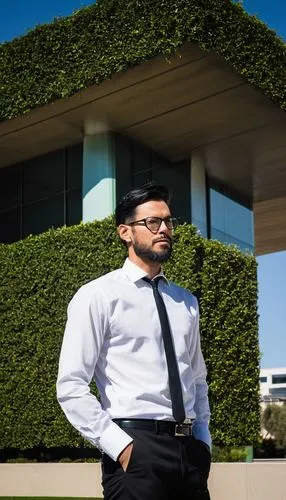 Male, mature, 30s, UCLAArchitectureGraduate, glasses, shortblackhair, beard, suit, white shirt, blacktie, blacktrousers, blackleather shoes, holding architectural model, standing, UCLA campus, modern 