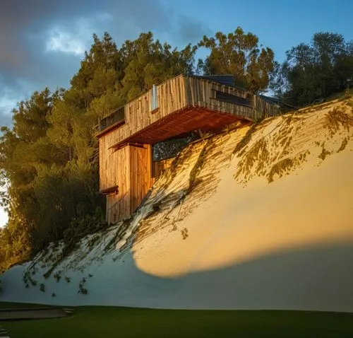 a wood cladding public building with artifial light and big windows at sundown cloudy sky located in a pine forest in the middle east ,a very cool looking house on the side of a hill,dunes house,dune 