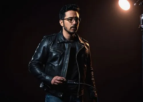 Dark media producer, male, 30s, black hair, stubble, glasses, leather jacket, denim jeans, boots, holding microphone, standing, dimly lit studio, dark background, spotlight, professional lighting, cin