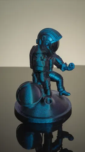 A blue astronaut figure is sitting on a black surface. The astronaut has a unique design and appears to be made  plastic in 3D printing. Build abstract scenes using geometric shapes that highlight the