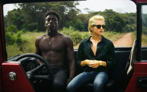 the boy has one hand on the steering wheel and the other on the gear shift of the Jeep.
The girl has a sweaty face and her blouse is open showing two gorgeous boobs.,man in sunglasses sitting behind d