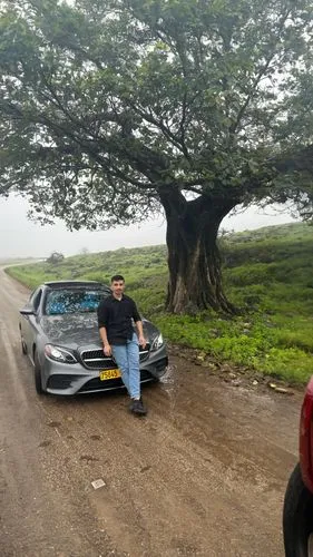 a man sitting in front of a car on a dirt road,salalah,purandar,panchgani,lonavla,tinian,waialua,dhofar,sinhagad,kilauea iki crater,mahabaleshwar,lonavala,rental car,koolau,matheran,haleakala,sinhgad,