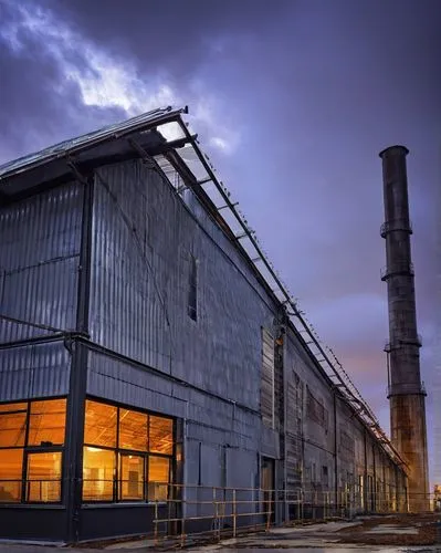 Industrial building, modern architecture, metallic structure, silver-gray corrugated iron sheets, curved roof, angular lines, urban cityscape, cloudy sky, dramatic lighting, low-angle shot, bold compo