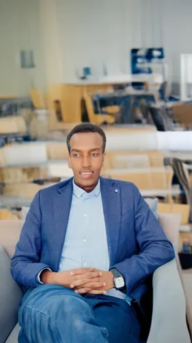 a man sitting on a chair looking into the camera,black businessman,african businessman,lennix,mekonnen,ceo,blur office background