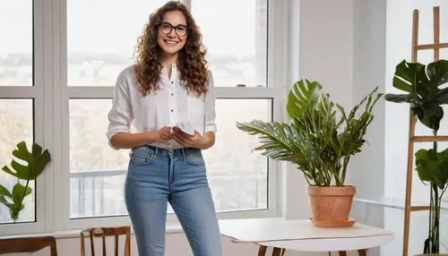 Female college student, interior design major, 20yo, long curly brown hair, glasses, elegant smile, white blouse, denim jeans, sneakers, holding a large portfolio, standing in a modern designed room, 