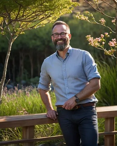 Brendan Bartlett, landscape architect, mature man, (40yo), short brown hair, glasses, beard, smiling, standing, outdoor, nature reserve, trees, bushes, flowers, hills, wooden fence, stone pathway, wat