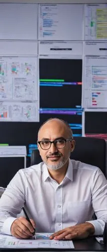 Software architect, middle-aged man, bespectacled, balding, wearing a white shirt, black trousers, sitting in front of a large desk with multiple monitors, holding a cup of coffee, pointing at a white